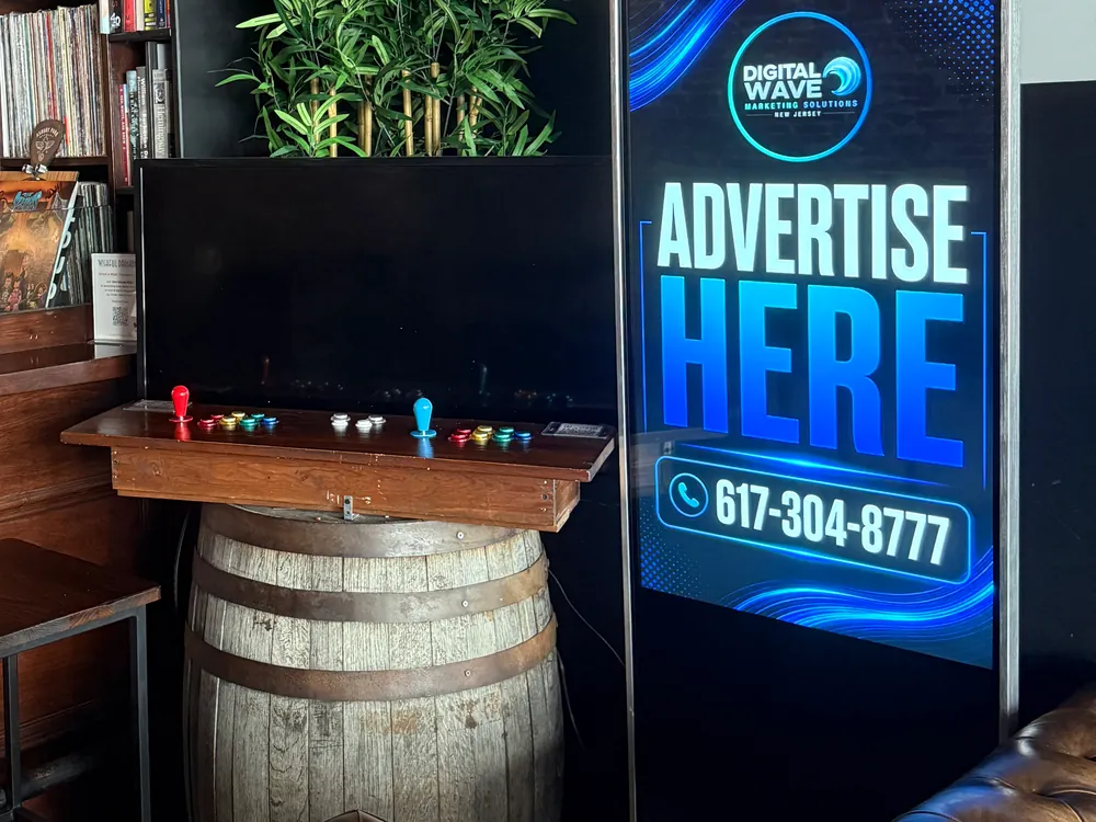 Digital Wave screen beside the arcade cabinet and barrel seating in an Asbury Park taproom