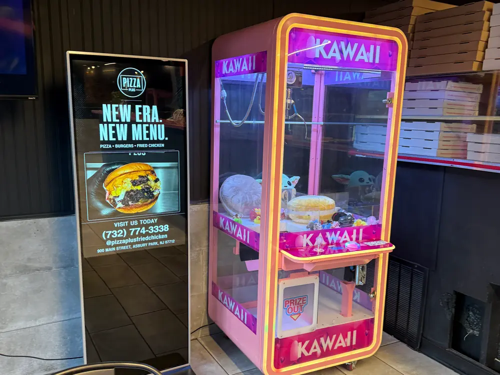 Floor-standing Digital Wave screen running a Pizza Plus ad beside the counter